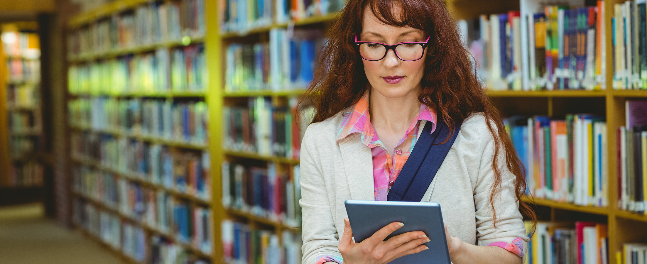 Professora em uma biblioteca olhando para um tablet